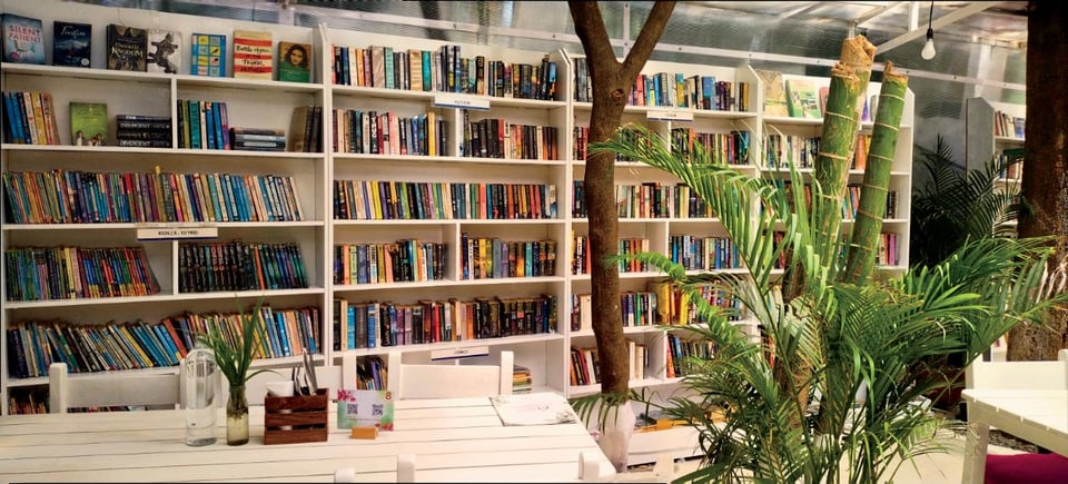 Bookshelves and white reading tables among plants at the Namma Ashram library